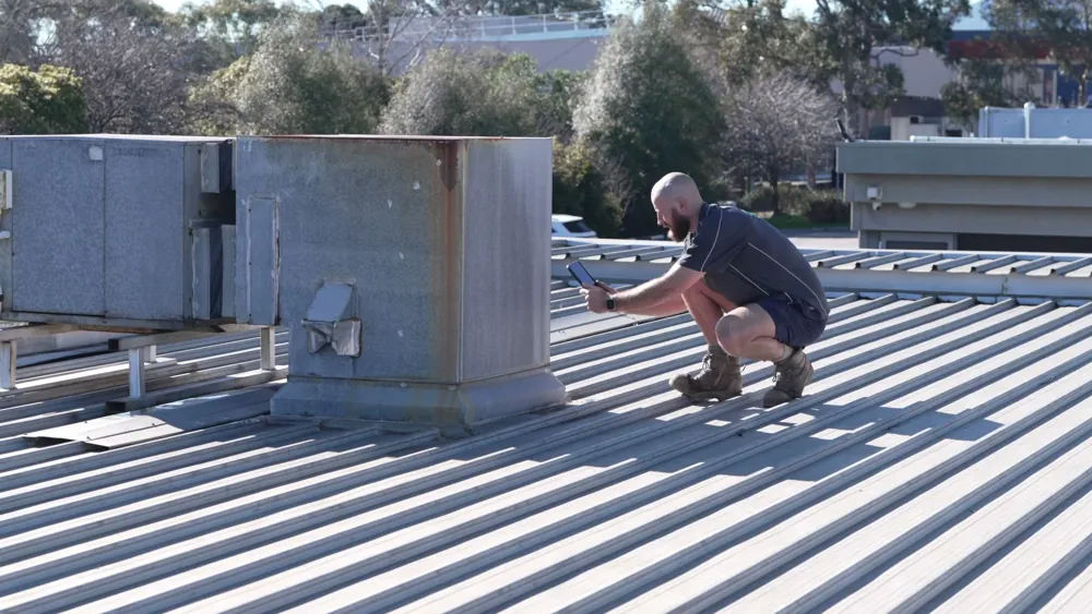 Roof plumber photographing around a rooftop unit to trace a leak