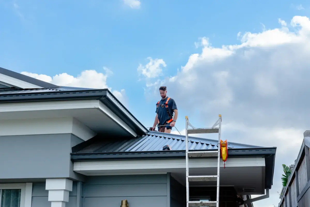 LifeProof roof plumber in a safety harness on a metal roof, ladder at the gutter