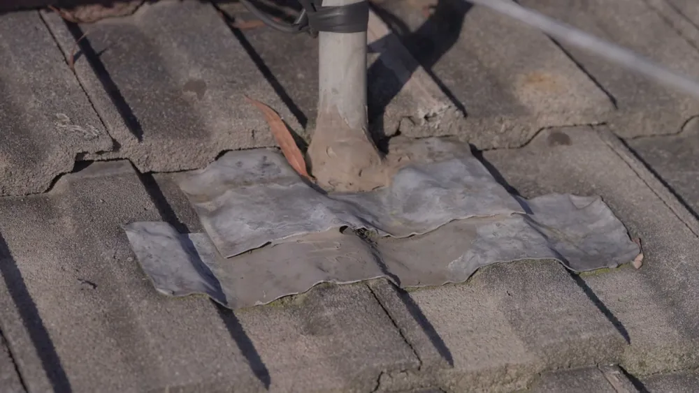 Old tape patches around a roof pipe on a concrete tile roof
