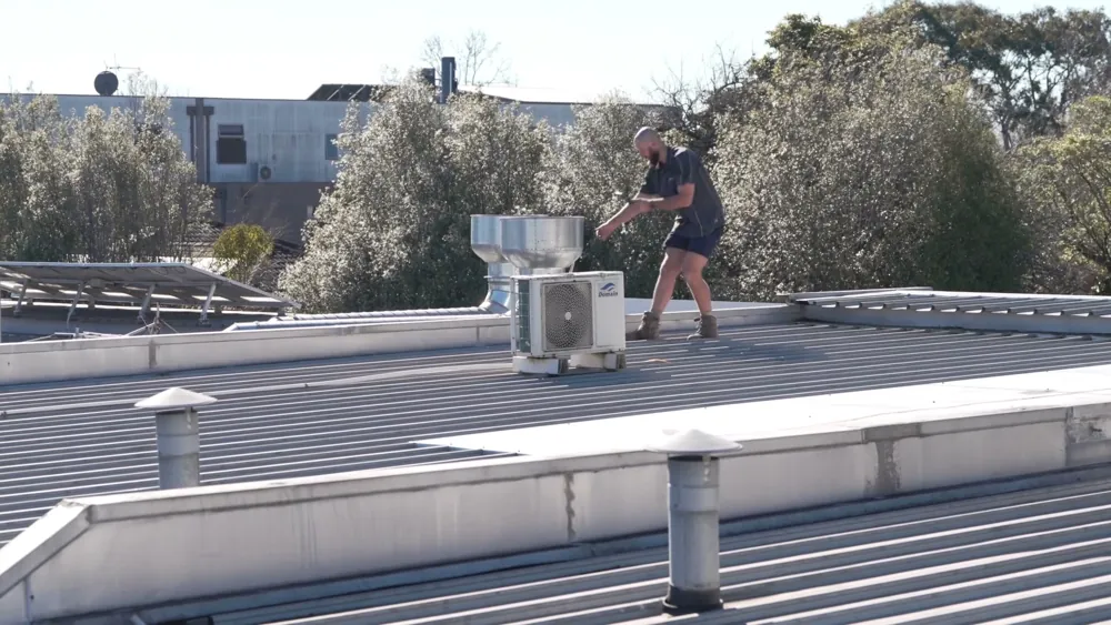 Roof plumber walking a flat metal roof to trace a leak