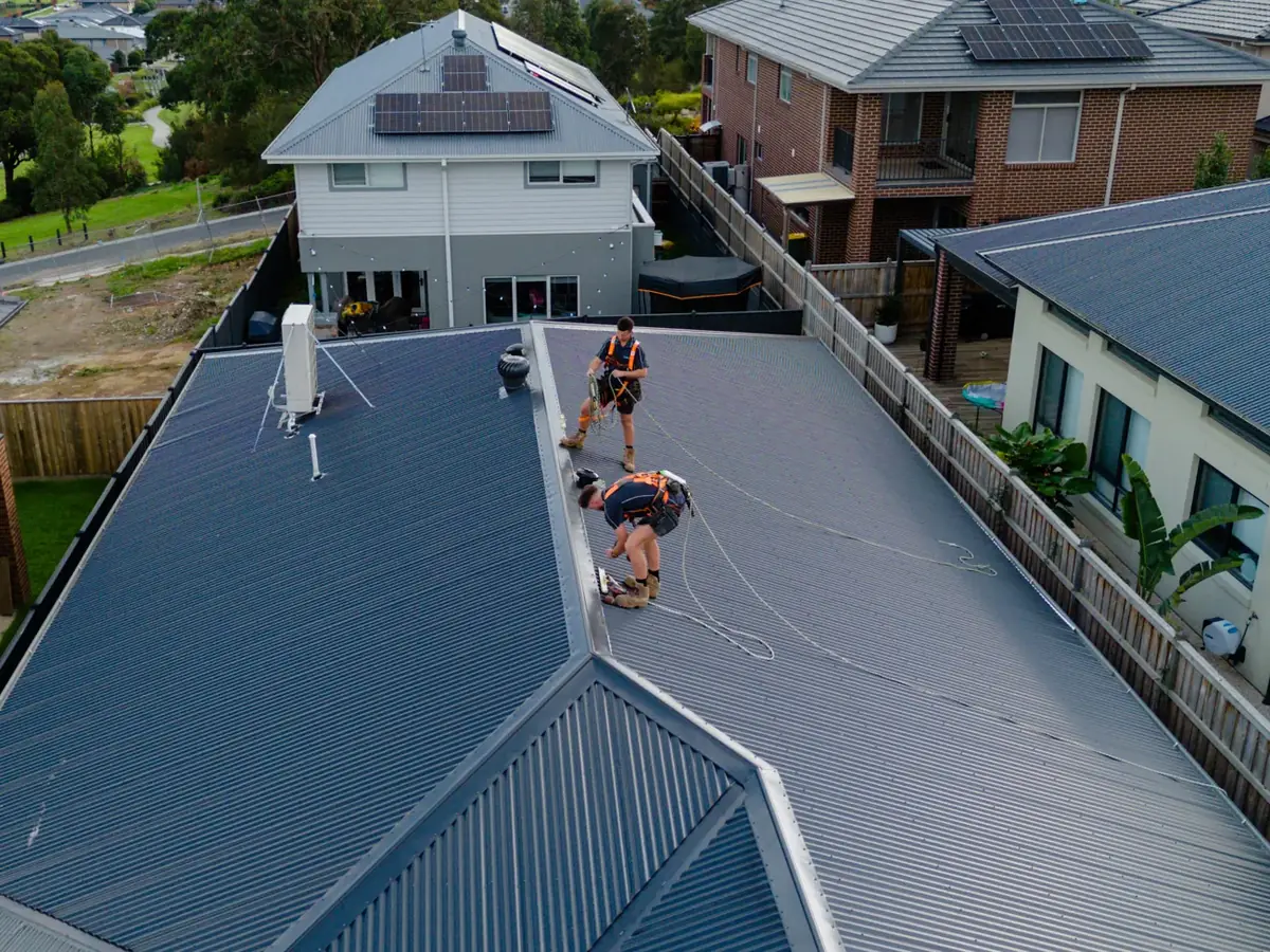 Two LifeProof roof plumbers in safety harnesses working on a new Colorbond roof, seen from above